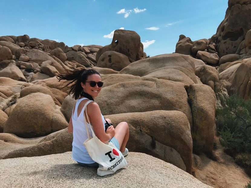 Girl sitting on a granite rock with a linen bag and sunglasses.
